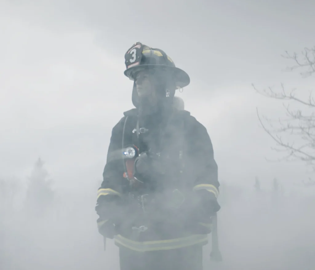Firefighter standing in thick smoke wearing protective gear.
